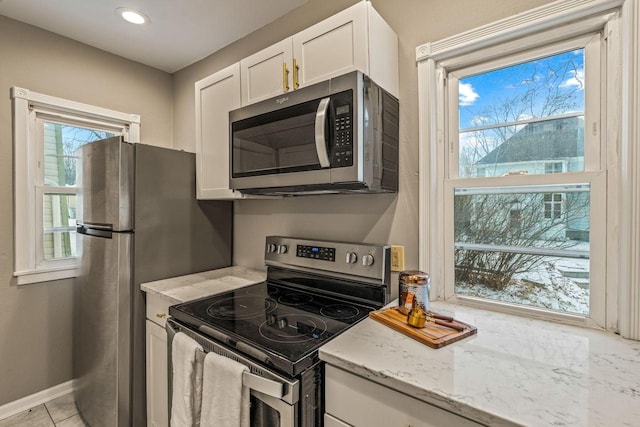 kitchen with a wealth of natural light, white cabinets, light stone counters, and appliances with stainless steel finishes