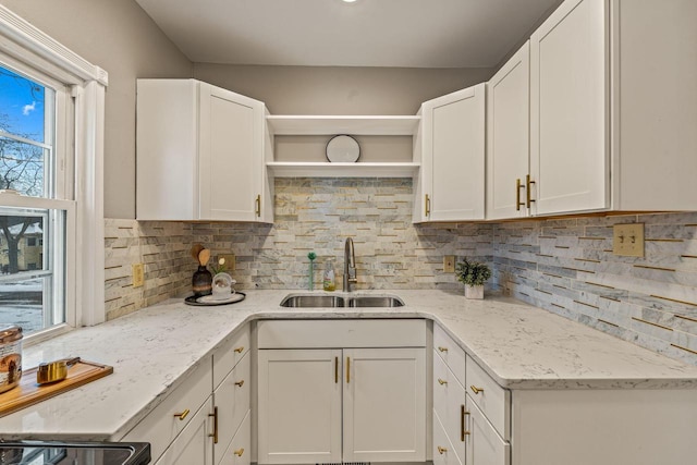 kitchen featuring tasteful backsplash, light stone counters, sink, and white cabinets