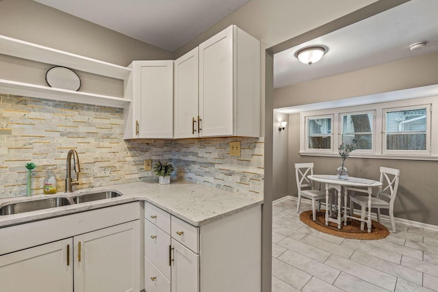 kitchen with white cabinets, backsplash, light stone counters, and sink