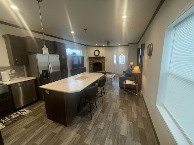 kitchen with pendant lighting, stainless steel appliances, a kitchen island, and dark wood-type flooring