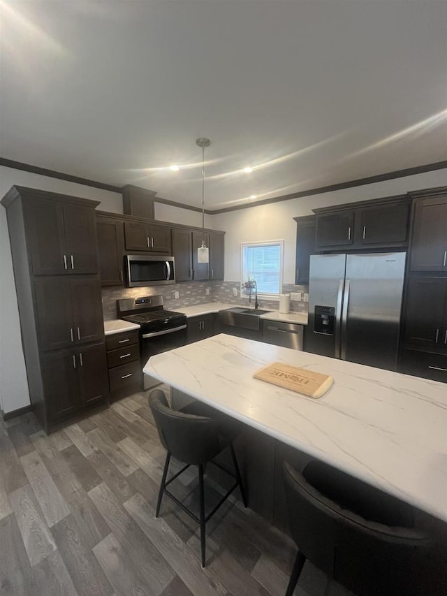 kitchen with pendant lighting, backsplash, sink, appliances with stainless steel finishes, and light hardwood / wood-style floors