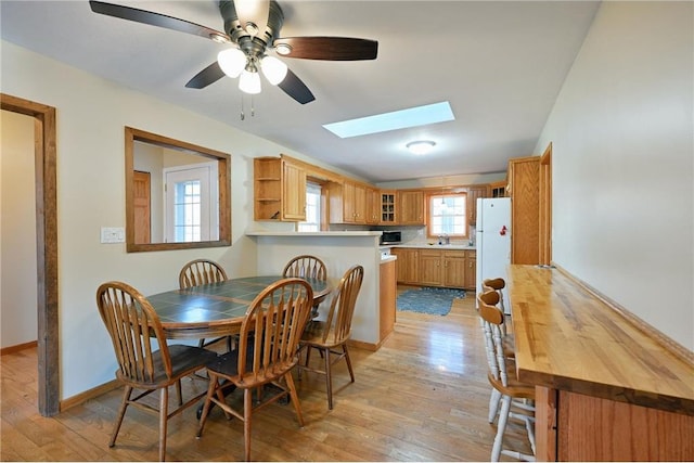 dining space featuring a skylight, ceiling fan, light hardwood / wood-style flooring, and sink