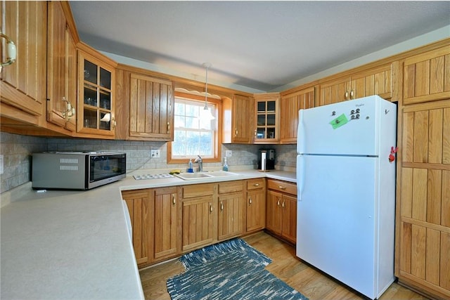 kitchen with decorative backsplash, light wood-type flooring, sink, pendant lighting, and white refrigerator