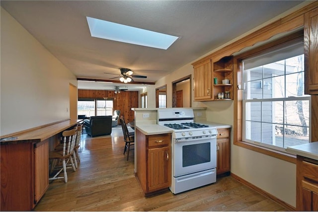 kitchen featuring white gas range, ceiling fan, a skylight, kitchen peninsula, and hardwood / wood-style flooring