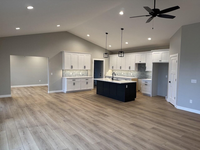 kitchen with ceiling fan, an island with sink, tasteful backsplash, decorative light fixtures, and white cabinetry