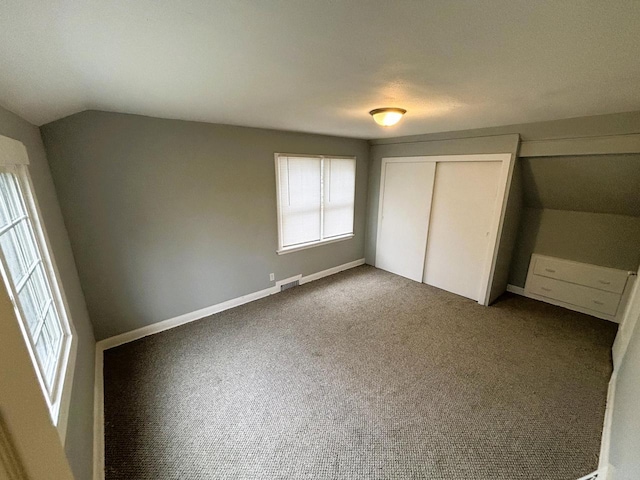 unfurnished bedroom featuring carpet flooring, vaulted ceiling, and a closet