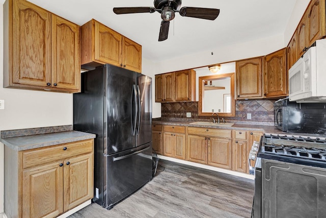 kitchen with backsplash, black fridge, gas stove, sink, and dark hardwood / wood-style floors