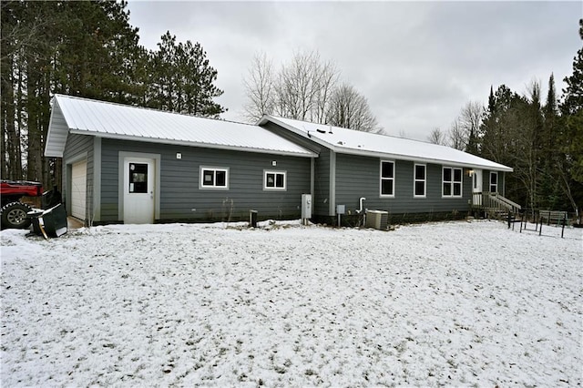 snow covered house featuring central air condition unit and a garage