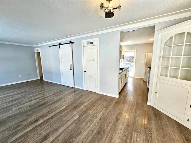 interior space with a textured ceiling, a barn door, dark hardwood / wood-style floors, and crown molding