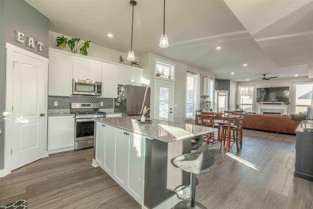 kitchen featuring light stone counters, hanging light fixtures, a kitchen island, white cabinets, and appliances with stainless steel finishes