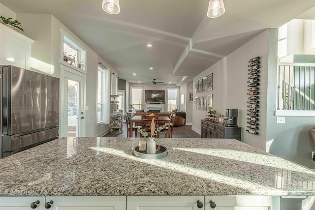 kitchen featuring ceiling fan, stainless steel fridge, white cabinetry, and light stone countertops