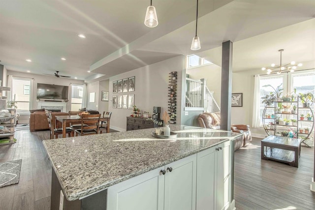 kitchen featuring light stone counters, dark wood-type flooring, hanging light fixtures, ceiling fan with notable chandelier, and white cabinets