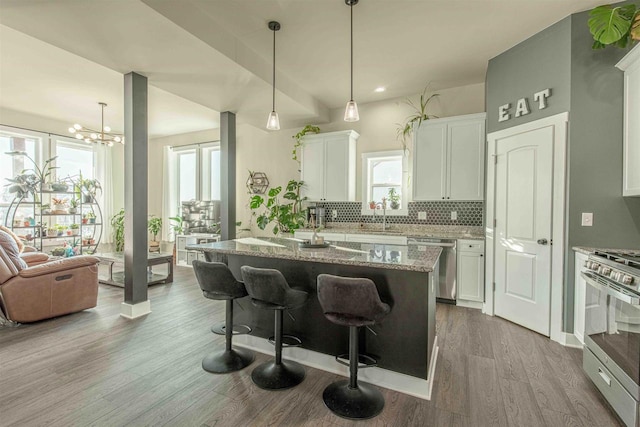 kitchen featuring a kitchen island with sink, a breakfast bar area, appliances with stainless steel finishes, light stone countertops, and white cabinets