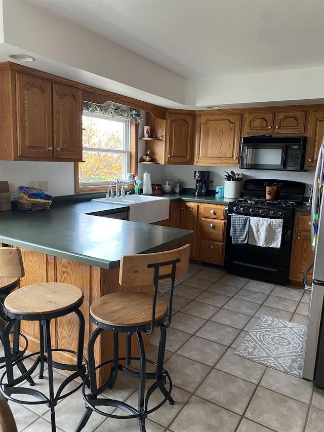 kitchen featuring sink, kitchen peninsula, a breakfast bar area, light tile patterned floors, and black appliances