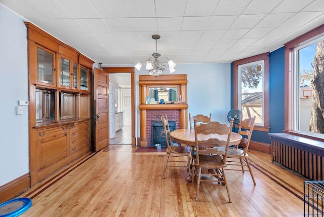 dining room with a fireplace, radiator heating unit, light hardwood / wood-style flooring, and a notable chandelier