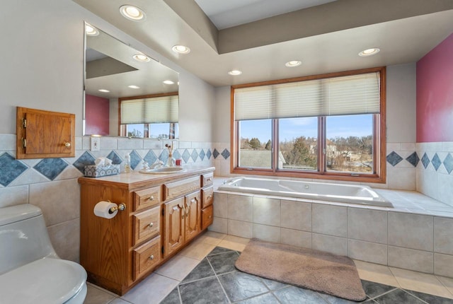 bathroom with a relaxing tiled tub, toilet, tile patterned floors, vanity, and tile walls