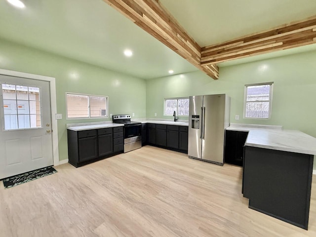 kitchen with kitchen peninsula, stainless steel appliances, sink, beam ceiling, and light hardwood / wood-style flooring