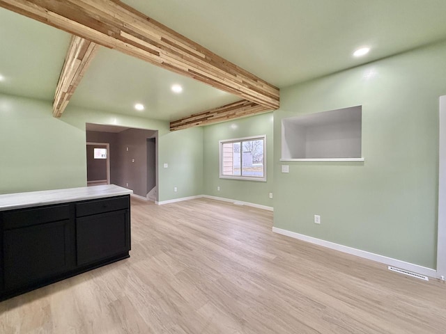 unfurnished living room with beamed ceiling and light wood-type flooring