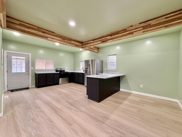 kitchen featuring kitchen peninsula, appliances with stainless steel finishes, light hardwood / wood-style flooring, and beamed ceiling