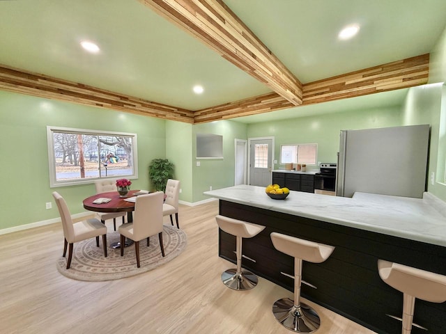 kitchen with light wood-type flooring, appliances with stainless steel finishes, beam ceiling, light stone counters, and kitchen peninsula