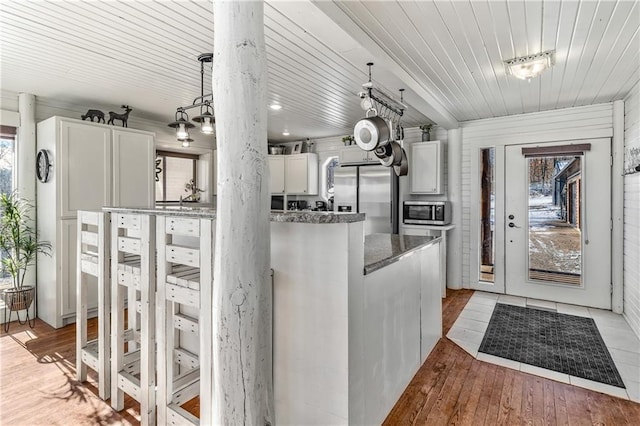 kitchen featuring stainless steel appliances, decorative light fixtures, light hardwood / wood-style flooring, dark stone countertops, and white cabinets