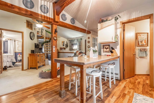 kitchen featuring ceiling fan, a baseboard radiator, light hardwood / wood-style flooring, lofted ceiling with beams, and a breakfast bar