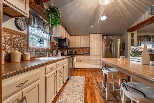 kitchen with appliances with stainless steel finishes, tasteful backsplash, sink, cream cabinetry, and light hardwood / wood-style floors