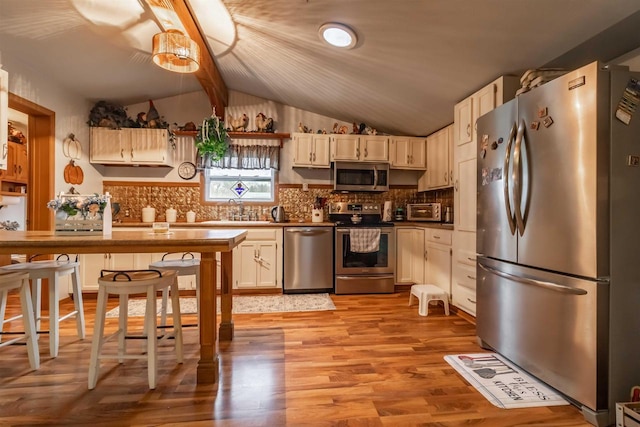 kitchen with decorative backsplash, lofted ceiling with beams, stainless steel appliances, and light hardwood / wood-style flooring