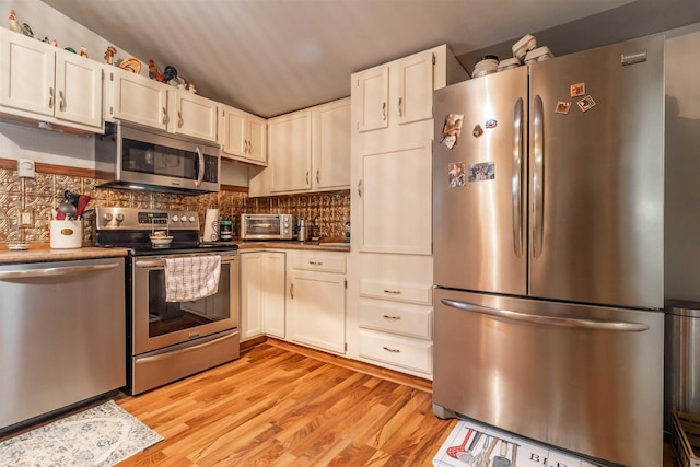 kitchen featuring lofted ceiling, light hardwood / wood-style flooring, appliances with stainless steel finishes, tasteful backsplash, and white cabinetry