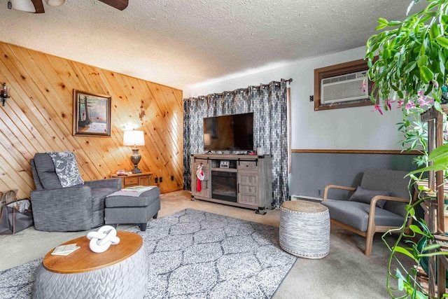 living room with a wall mounted air conditioner, wood walls, light carpet, ceiling fan, and a textured ceiling