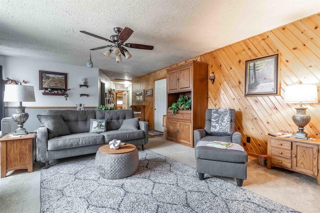 living room featuring wood walls, ceiling fan, light carpet, and a textured ceiling