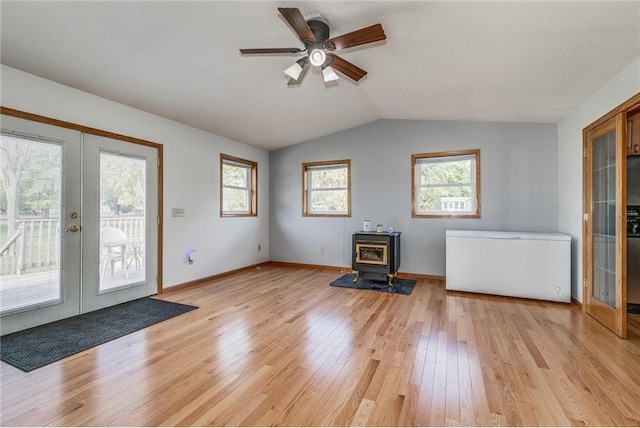 unfurnished living room with a wood stove, french doors, plenty of natural light, lofted ceiling, and light wood-type flooring