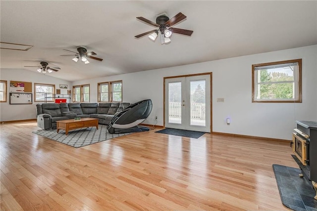 living room featuring french doors, light wood-type flooring, a wood stove, and vaulted ceiling