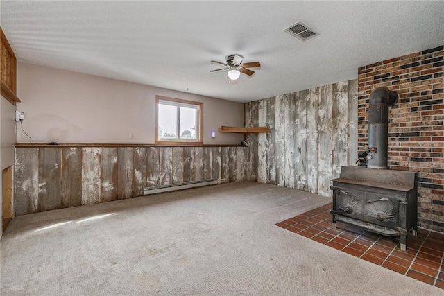 unfurnished living room featuring a wood stove, ceiling fan, dark colored carpet, a baseboard heating unit, and a textured ceiling