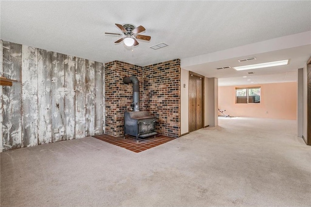 unfurnished living room with a wood stove, ceiling fan, carpet floors, and a textured ceiling