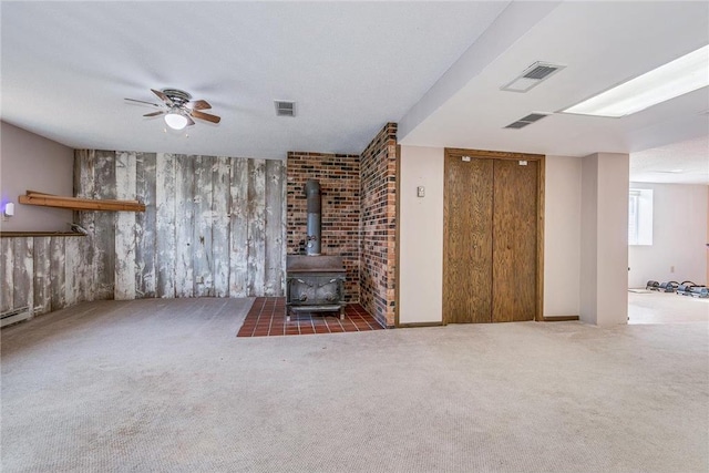 unfurnished living room with dark colored carpet, ceiling fan, a wood stove, and a textured ceiling