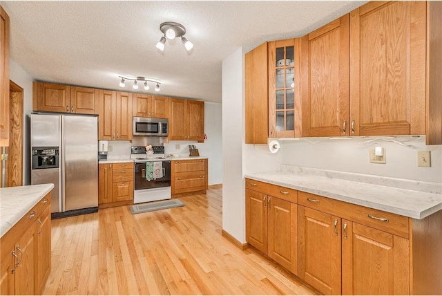 kitchen featuring light stone counters, light wood-type flooring, a textured ceiling, and appliances with stainless steel finishes