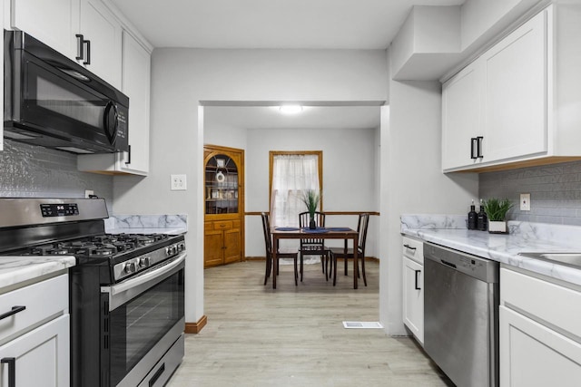 kitchen featuring light stone counters, light hardwood / wood-style flooring, white cabinets, and appliances with stainless steel finishes