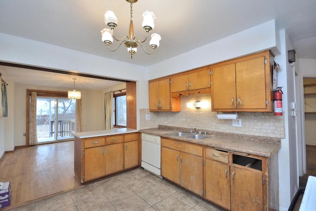 kitchen featuring kitchen peninsula, white dishwasher, sink, a chandelier, and hanging light fixtures