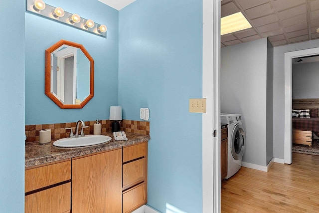 bathroom featuring decorative backsplash, a drop ceiling, vanity, washer and clothes dryer, and wood-type flooring