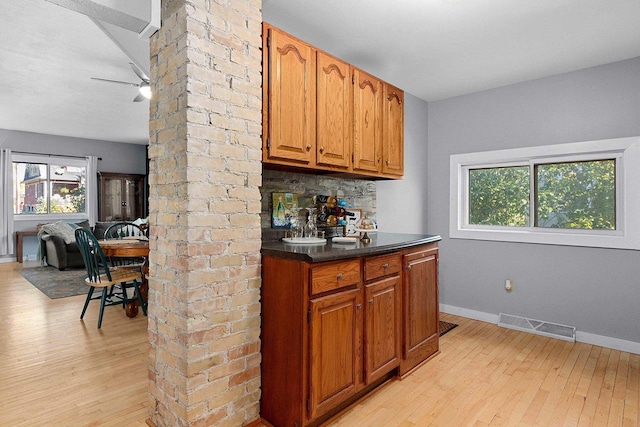 bar with ornate columns, decorative backsplash, ceiling fan, and light hardwood / wood-style floors