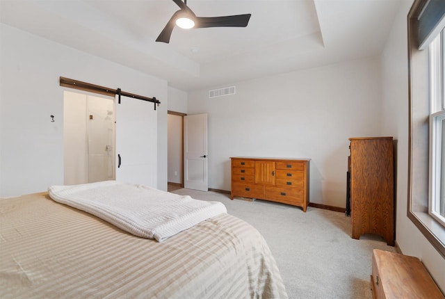 bedroom with light carpet, a tray ceiling, ceiling fan, a barn door, and multiple windows