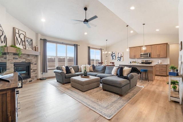 living room with ceiling fan with notable chandelier, a stone fireplace, light wood-type flooring, and lofted ceiling