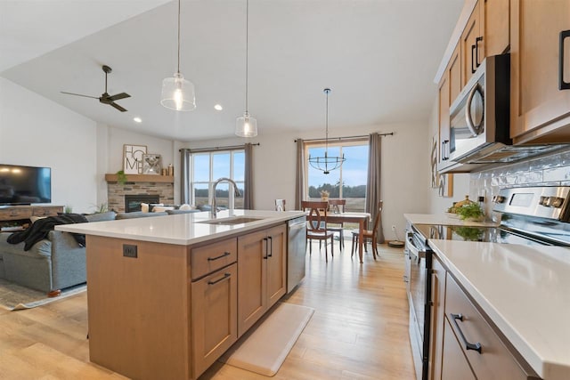 kitchen featuring a center island with sink, a stone fireplace, sink, vaulted ceiling, and appliances with stainless steel finishes