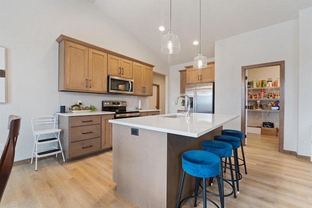 kitchen with sink, pendant lighting, a kitchen bar, a kitchen island with sink, and appliances with stainless steel finishes