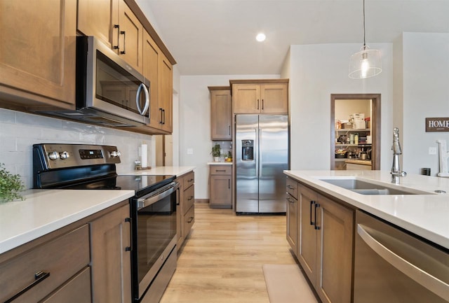 kitchen with sink, stainless steel appliances, tasteful backsplash, light hardwood / wood-style floors, and decorative light fixtures