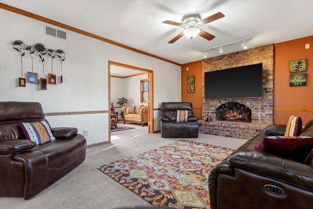 living room featuring track lighting, crown molding, ceiling fan, a fireplace, and light colored carpet