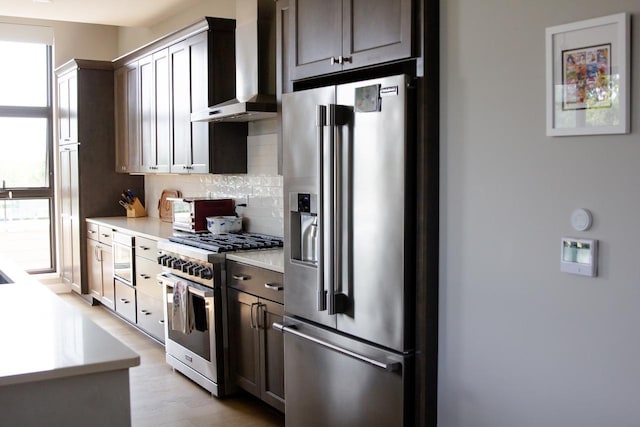 kitchen featuring wall chimney exhaust hood, decorative backsplash, a wealth of natural light, dark brown cabinets, and stainless steel appliances