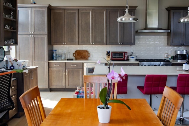 kitchen with dark brown cabinetry, stove, hanging light fixtures, and wall chimney range hood