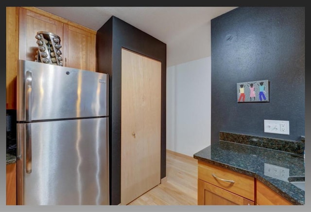 kitchen with dark stone countertops, stainless steel refrigerator, and light hardwood / wood-style flooring